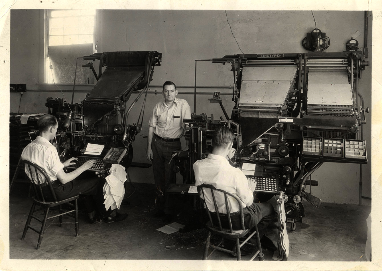 Photograph of three men, two working at linographs